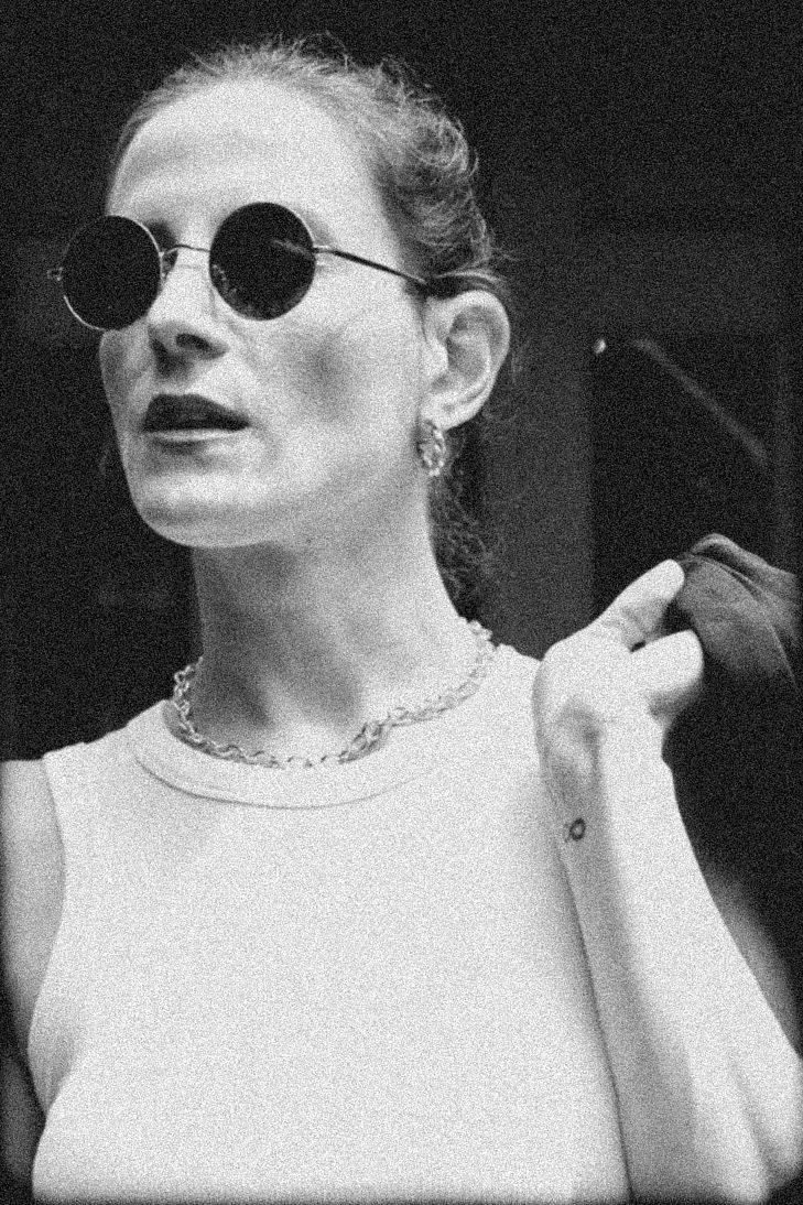 Black and white film-grain portrait of Gabriela in a white tank and round sunglasses
