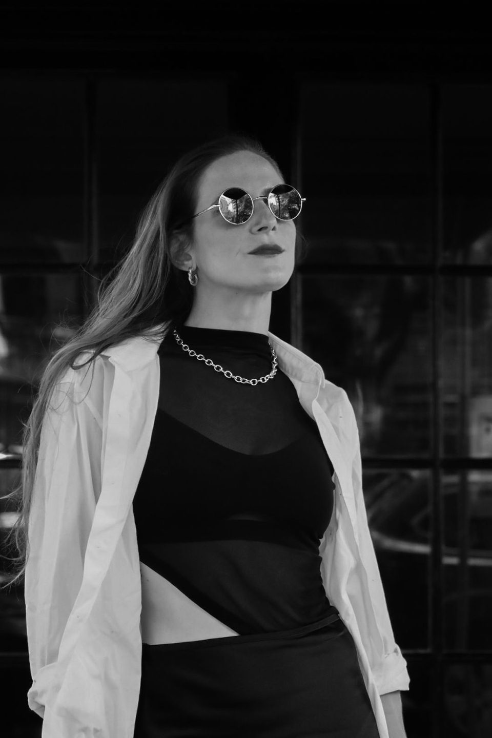 Black and white. A white shirt over a sheer black top, gold chain, looking up.