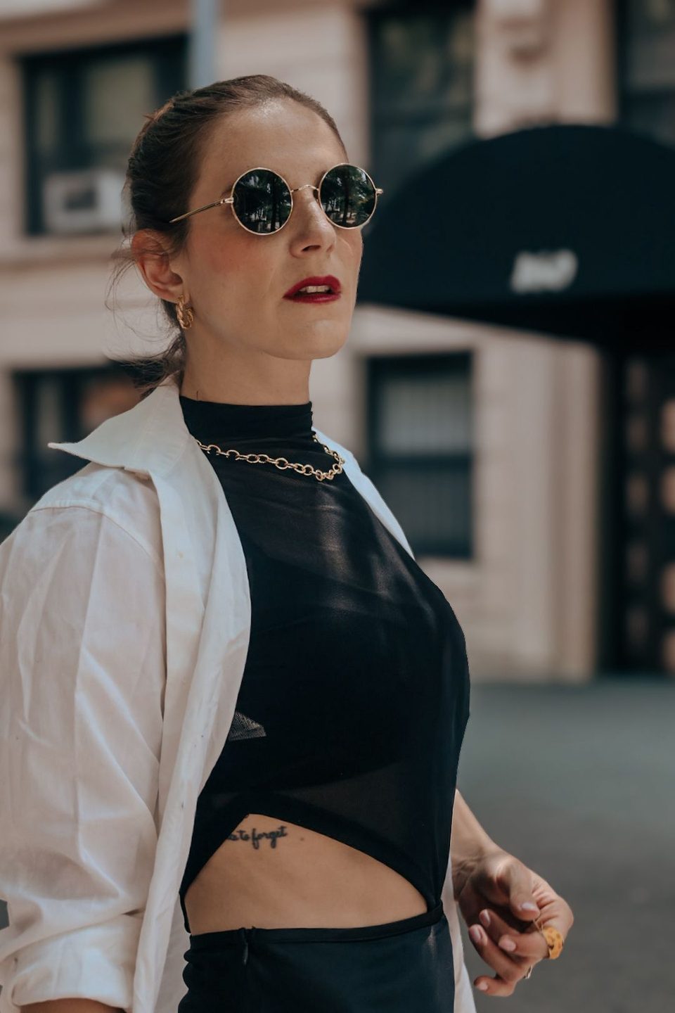 A white shirt over a sheer black top, hair slicked back, looking off camera.