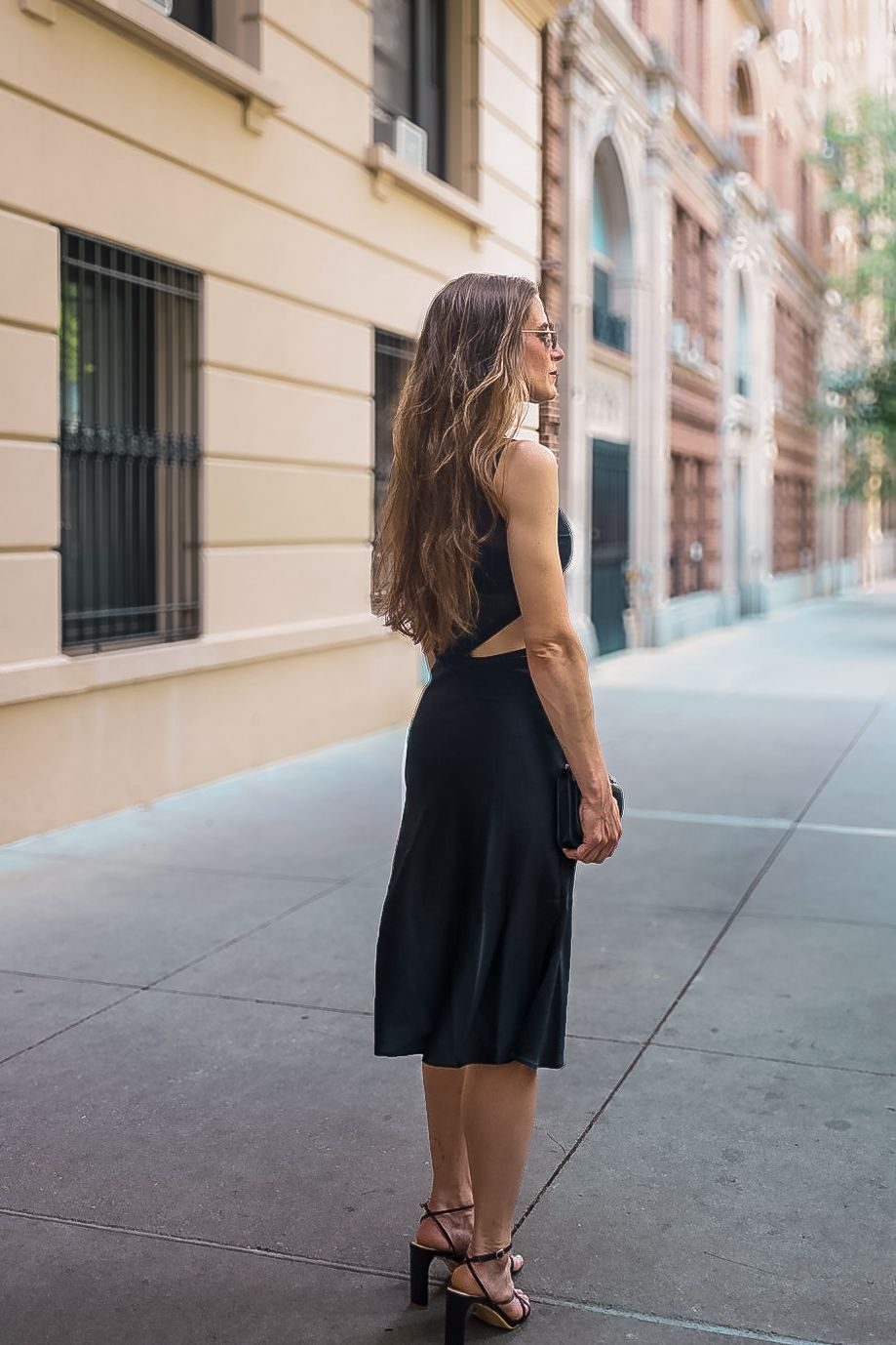 Seen from behind on a sidewalk, black slip skirt and strappy sandals, hair down her back.