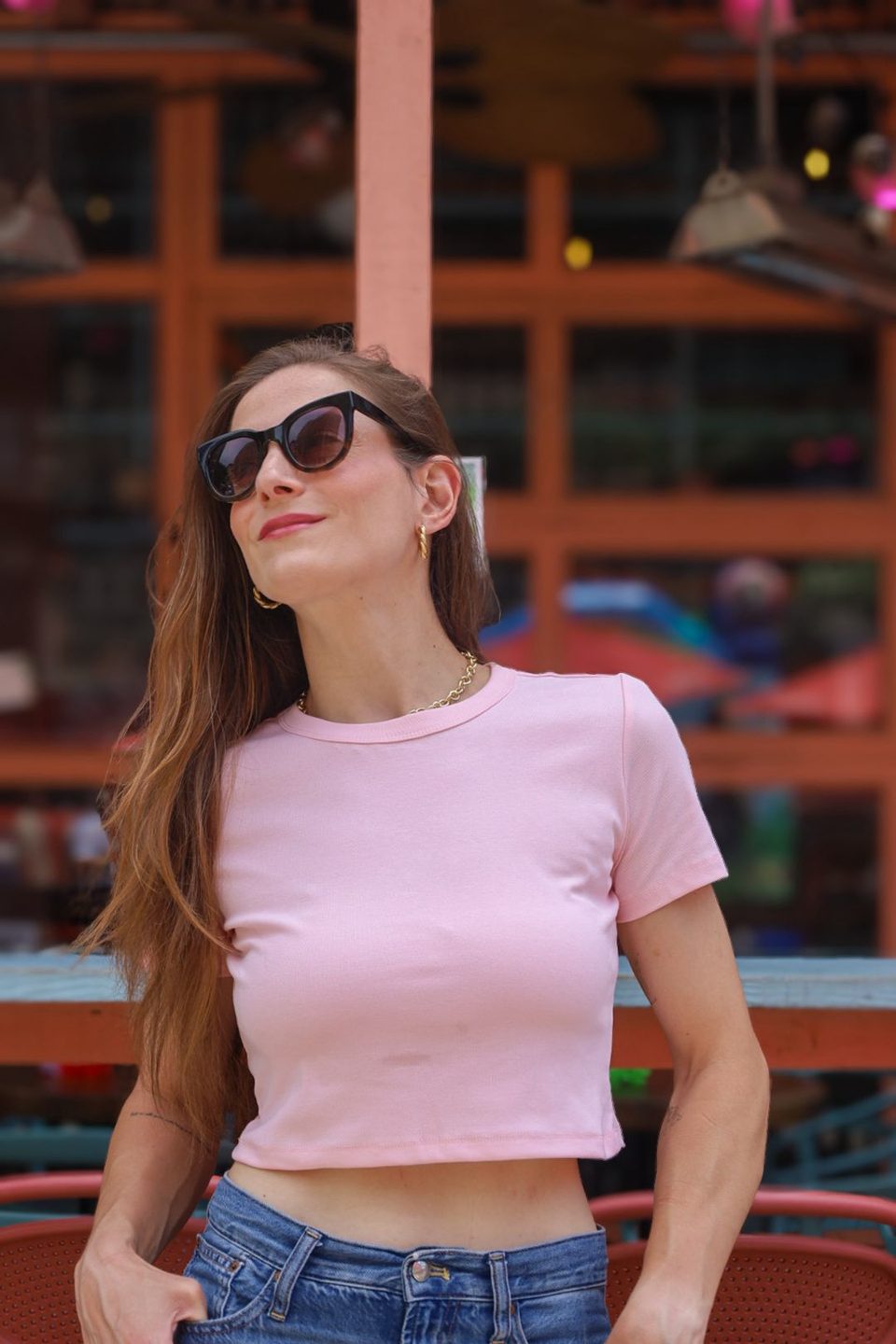 Pink tee and cat eye sunglasses, hand in pocket, looking up.