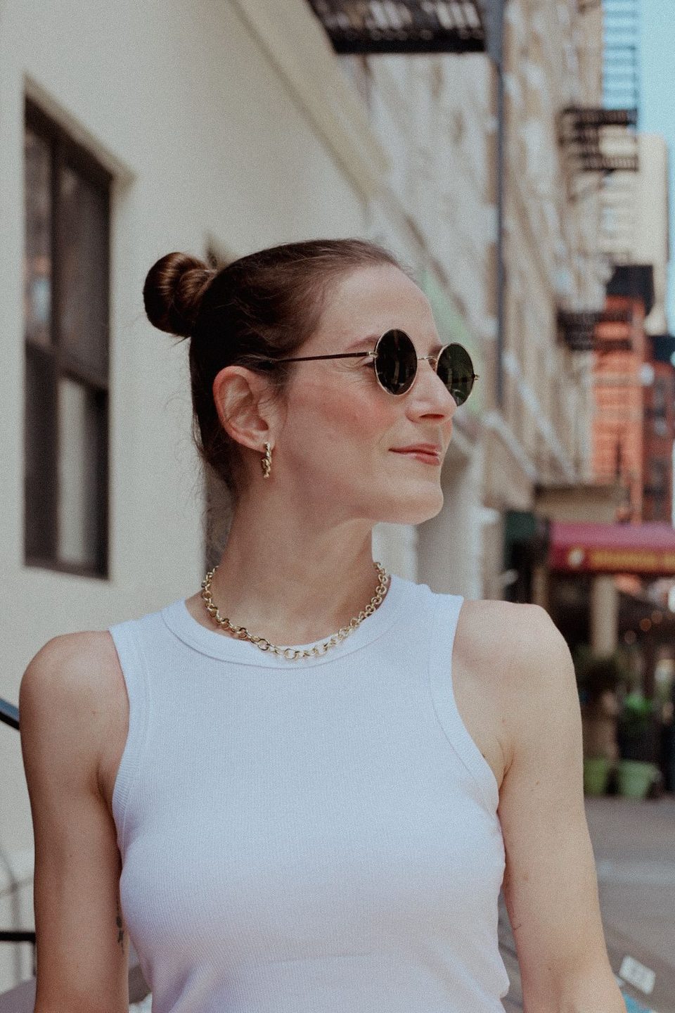 Profile smile, hair up in two buns, white tank and gold chain.