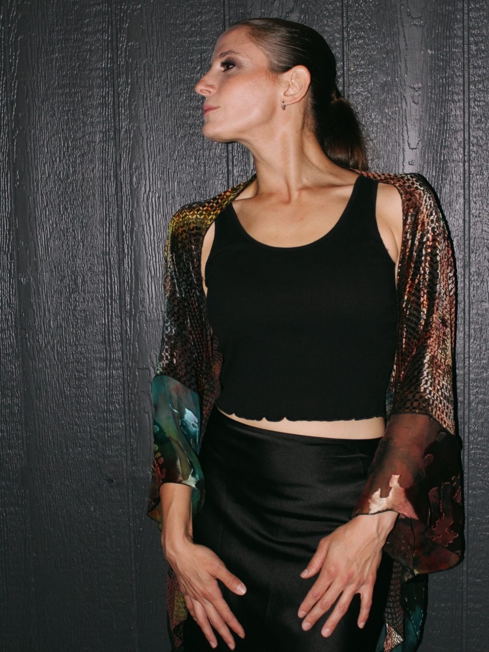 Black crop top and satin skirt under silk shibori, looking over her shoulder.